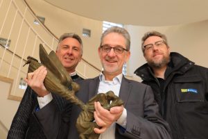 Aus dem Archiv zurück im Stadthaus 1: Stadtrat Matthias Peck hält den Engel, der wieder an seinem angestammten Platz im Treppenturm des Stadthauses 1 wacht. Siegfried Methner und Daniel Bracht (re.), Projektleiter der Stadthaus-Sanierung, unterstützen beim Befestigen der Skulptur. (Foto: Stadt Münster / Presseamt)