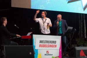 Jovel-Chef Marvin Lindenberg (Mitte) dirigiert die Rudelsinger und den Pianisten beim Weltrekordversuch. Rechts im Bild: Rudelsingen-Erfinder David Rauterberg. (Foto: cb)