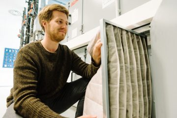 EPA-Filter sind besonders feine Taschenfilter, die selbst feine Aerosole filtern können. Der wissenschaftliche Mitarbeiter Steffen Jacobs baut hier einen neuen Filter in eine Klimaanlage ein. (Foto: FH Münster/Maxi Krähling)