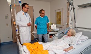 Prominenter Aushilfspfleger am Freiwilligentag: Jörg Adler (m.) mit dem ärztlichen Leiter der Palliaitvstation, Dr. Marc Theisen am Bett von Barbara Zimmermann. (Foto: Raphaelsklink)