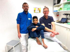 Dr. Eckhard Maicher (re.), Chefarzt der Kinder- und Neuroorthopädie, und Alexander Müller, Orthopädietechniker bei Orthopädie Technik Menßen, freuen sich gemeinsam mit Franco über den Erfolg der Klumpfuß-OP. (Foto: St. Franziskus-Hospital)