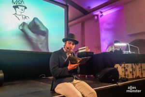 Schauspieler Ari Nadkarni trug in der Friedenskapelle Auszüge aus dem Roman "Der große Gatsby" vor, während Robert Nippoldt (rechts hinter der Lampe) Zeichnungen dazu anfertigte. (Foto: Ralf Clausen)