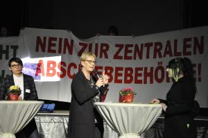 Beim Neujahrsempfang der Grünen protestierten Aktivisten gegen die Einrichtung einer ZAB in Münster und entrollten Transparente. Mit im Bild sind die Grünen-Politikerinnen Josefine Paul (li.) und Maria Klein-Schmeink (Bildmitte). (Foto: No ZAB)